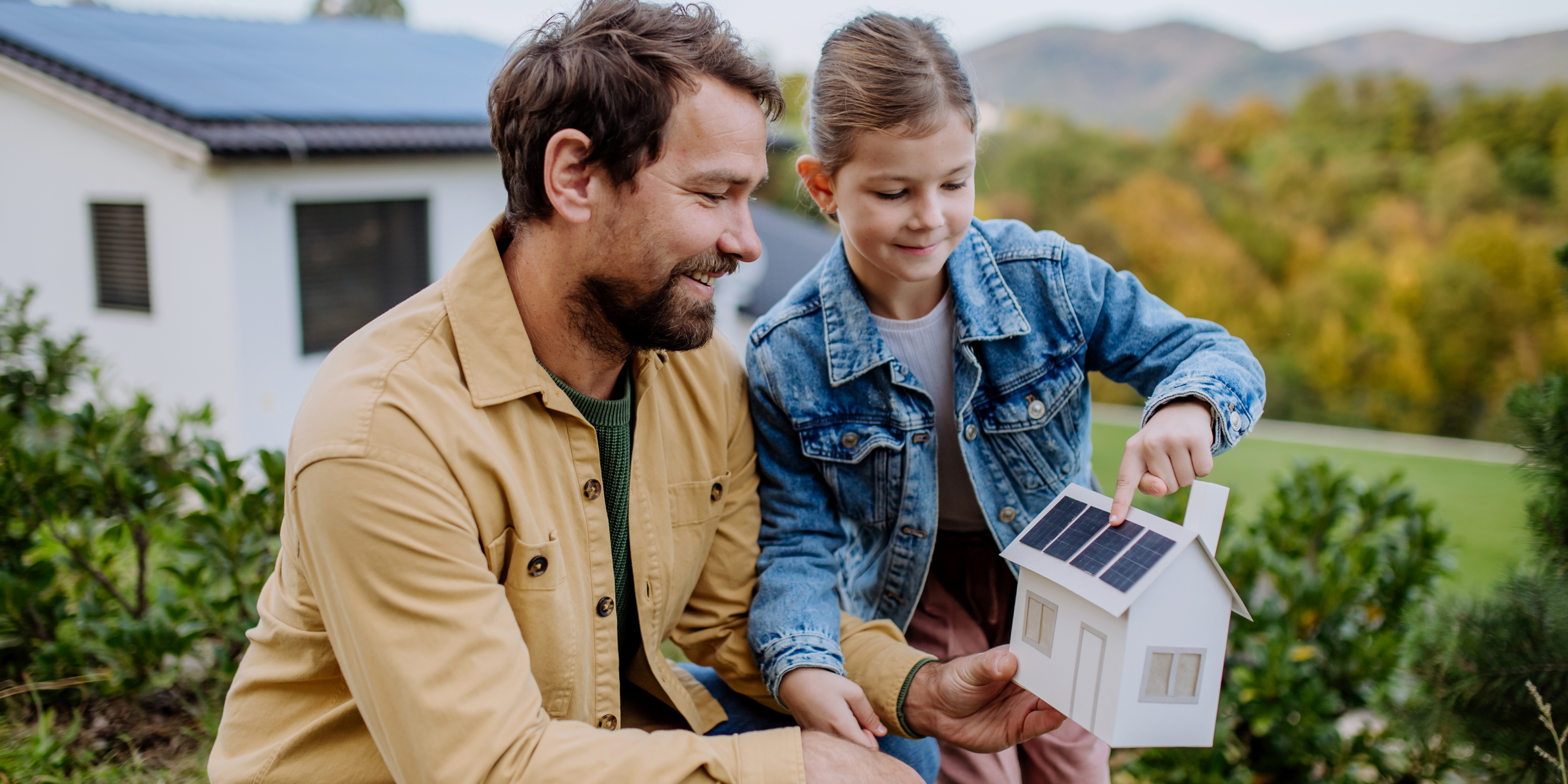 A father and his daughter holding a model home with solar panels. 